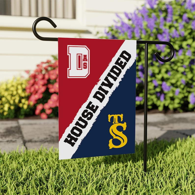 K&ouml;nnte beinhalten: Eine rot-blaue Gartenflagge mit einer wei&szlig;en Diagonalen. Der Text "HOUSE DIVIDED" ist auf der wei&szlig;en Linie geschrieben. Die obere H&auml;lfte der Flagge zeigt ein wei&szlig;es "D" mit den Buchstaben "AS" darin. Die untere H&auml;lfte der Flagge zeigt ein gelbes "S" mit einem "T" dar&uuml;ber.