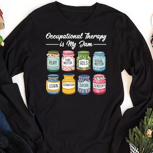 May include: Black long-sleeve t-shirt with the text "Occupational Therapy - is My Jam -" and a graphic of nine colorful jars with words like "Play", "Fine Motor", "ADLs", "Visual Motor", "Learn", "Cognition", "Social", and "Sensory".