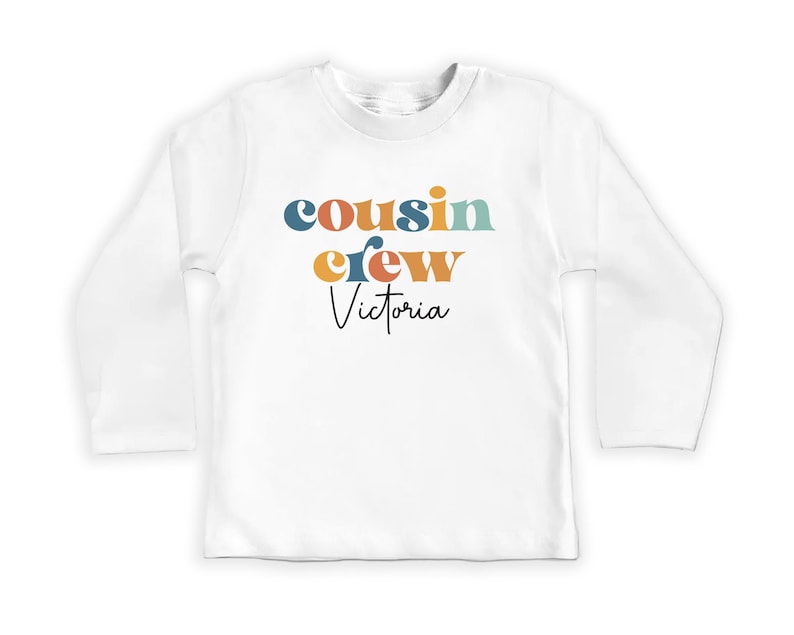 May include: White long-sleeve shirt with the text "cousin crew Victoria" in colorful retro-style lettering.