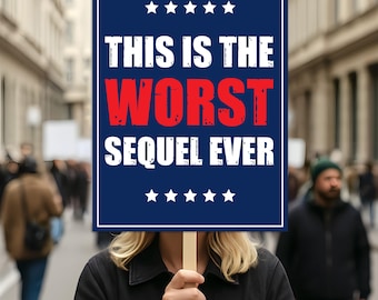 Pode incluir: Uma pessoa segurando uma placa com o texto "THIS IS THE WORST SEQUEL EVER" em letras brancas e vermelhas sobre um fundo azul marinho. A placa tem estrelas brancas na parte superior e inferior. A pessoa está em uma multidão.