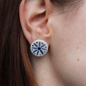 May include: A pair of white ceramic earrings with a blue starburst design.