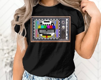 May include: Black t-shirt with a vintage television screen graphic featuring a color test pattern. The television screen is surrounded by a brown wooden frame.