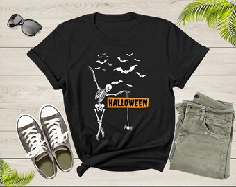May include: Black t-shirt with a skeleton dancing and holding a sign that says "Halloween". There are bats flying around the skeleton.