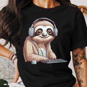 May include: Black t-shirt featuring a cartoon sloth wearing headphones and typing on a keyboard. The sloth has brown fur and a light brown face with black eyes. The headphones are gray and the keyboard is black.
