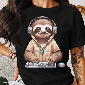 May include: Black t-shirt with a graphic of a sloth wearing headphones and typing on a keyboard. The sloth is wearing a brown shirt with a pocket and a lanyard.