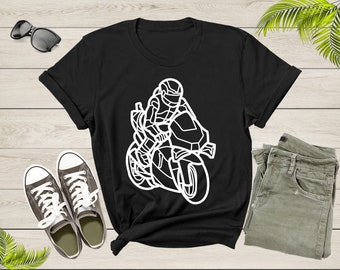 May include: Black t-shirt featuring a white graphic of a motorcyclist on a racing motorcycle. The design shows the rider in a helmet and protective gear. The shirt is displayed with sunglasses, sneakers, and olive-green pants on a wooden surface.
