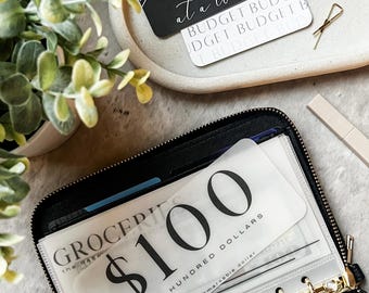 May include: A black leather planner with gold rings and a clear plastic pocket containing a white card with the text "$100 ONE HUNDRED DOLLARS the RAEmarkabie dollar".