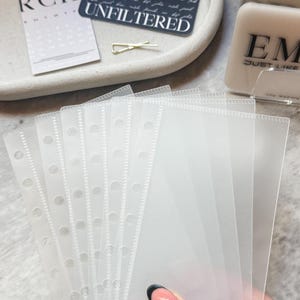 May include: A stack of clear plastic sleeves with holes for a binder. The sleeves are designed to hold and protect papers or cards.