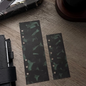 May include: Two rectangular planner inserts featuring a dark green and black mottled pattern. Each insert has a vertical row of circular punched holes along one side for binding, designed for use in a personal organizer or binder system.
