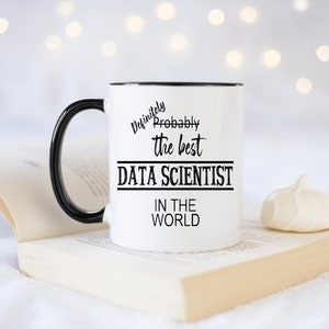 May include: White ceramic mug with a black handle and black rim. The mug has black text that reads "Definitely Probably the best DATA SCIENTIST in the WORLD".