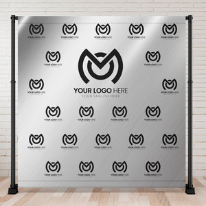 May include: A silver backdrop with a black and white logo repeated throughout. The logo is a stylized letter "M" with a circle inside. The text "YOUR LOGO HERE" and "YOUR TAGLINE HERE" is printed in black at the centre of the backdrop.