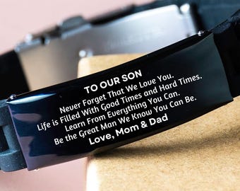 Op de afbeelding: Zwarte siliconen armband met een zilveren metalen sluiting en een zwarte metalen plaat met de gravure "To Our Son Never Forget That We Love You. Life is Filled With Good Times and Hard Times. Learn From Everything You Can. Be the Great Man We Know You Can Be. Love, Mom & Dad"