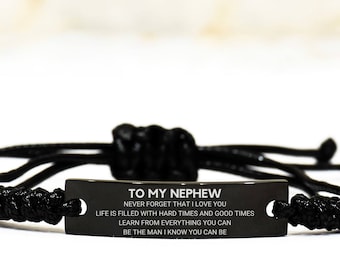 May include: Black adjustable bracelet with a rectangular metal plate. The plate has the text "TO MY NEPHEW" and an inspirational message. The bracelet is made of woven black cord.