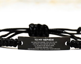 May include: Black braided bracelet with a rectangular black metal plate. The plate has white text that reads "TO MY NEPHEW" and a message. The bracelet is adjustable. The background is white.