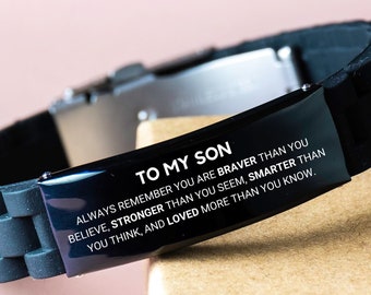 Op de afbeelding: Zwarte siliconen armband met een zilveren metalen plaat met de gravure "Aan mijn zoon, onthoud altijd dat je dapperder bent dan je denkt, sterker dan je lijkt, slimmer dan je denkt en meer geliefd dan je weet."
