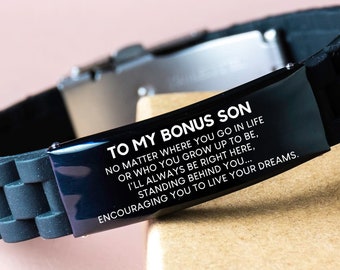 Op de afbeelding: Zwart siliconen armband met een roestvrijstalen sluiting. De armband heeft een zwarte rechthoekige plaat met de tekst "TO MY BONUS SON" en een bemoedigende boodschap. Een attent cadeau.