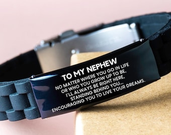 May include: Black silicone bracelet with a stainless steel clasp. The bracelet features a black metal plate with the text "TO MY NEPHEW" and an inspirational message. The bracelet is displayed on a light brown surface.