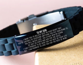 Op de afbeelding: Een zwarte siliconen armband met een zilveren metalen insert. De insert is gegraveerd met een boodschap die luidt: "Aan mijn zoon, ik wil dat je diep in je hart gelooft dat je alles kunt bereiken wat je je voorneemt. Je zult nooit verliezen, je wint of je leert, dus ga gewoon door en streef naar de sterren. Ik kan je niet beloven om er voor de rest van je leven te zijn, maar ik kan je beloven om van je te houden voor de rest van mijn leven."