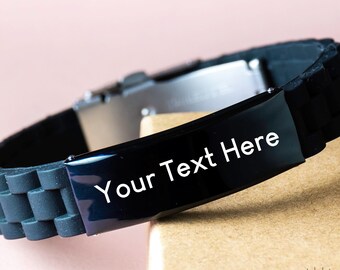 May include: Black silicone bracelet with a silver clasp and a black metal plate engraved with the text "Your Text Here".