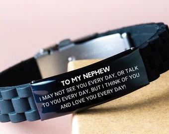 May include: Black silicone bracelet with a stainless steel clasp. The black metal plate is engraved with the text "TO MY NEPHEW" and a loving message. The bracelet is displayed on a light brown surface.