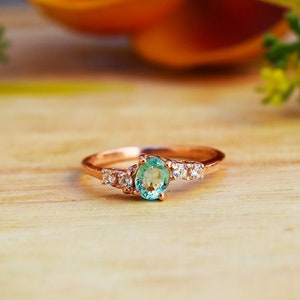 May include: A rose gold ring featuring a light green oval gemstone and smaller clear gemstones set in a delicate band.
