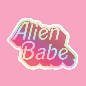 Op de afbeelding: Een sticker met een holografisch effect met de tekst "Alien Babe" in een roze, blauwe en groene kleurstelling.