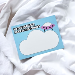 May include: A blue card with the text "NOTES FROM MY HEAD IN THE CLOUDS" and a pink and black UFO flying over a white cloud.