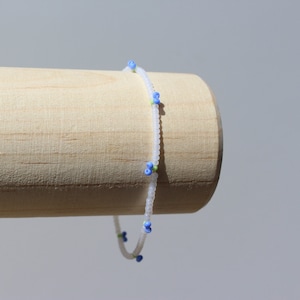 May include: A white beaded bracelet with small blue and green flower accents.