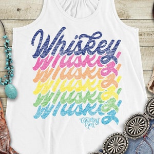 May include: White tank top with a rainbow design of the word "Whiskey" repeated multiple times. The tank top has a scoop neck and a relaxed fit. The tank top is styled with a turquoise necklace, brown cowboy boots, a silver belt buckle, and blue jeans.