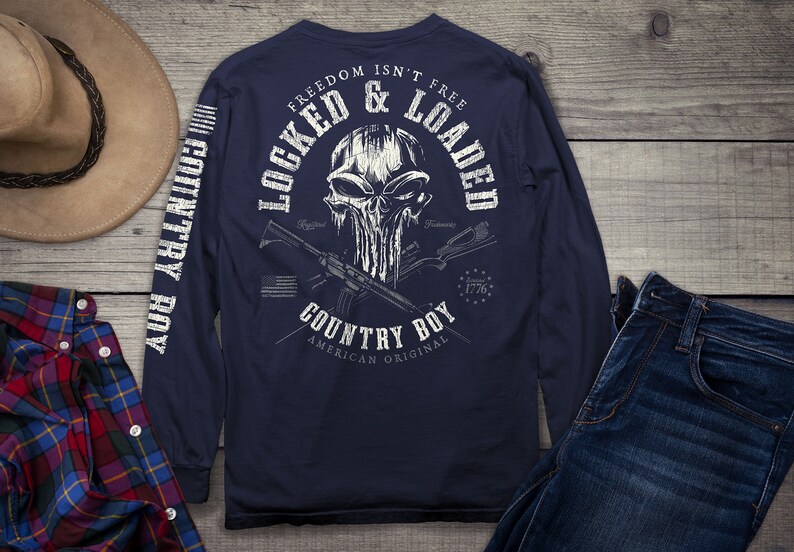 Op de afbeelding: Een marineblauw shirt met lange mouwen met een witte schedelprint en de tekst "Freedom Isn't Free Locked & Loaded Country Boy American Original 1776". De mouwen hebben de tekst "Country Boy" verticaal gedrukt.