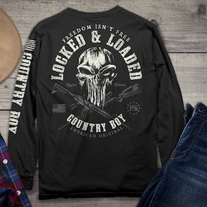 Op de afbeelding: Zwart langarm shirt met een witte schedel afbeelding en de tekst "Freedom Isn't Free Locked & Loaded Country Boy American Original" op de rug. De mouwen hebben de tekst "Country Boy" verticaal gedrukt.
