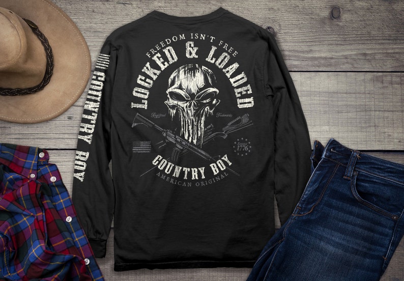 Op de afbeelding: Zwart langarm shirt met een witte schedel afbeelding en de tekst "Freedom Isn't Free Locked & Loaded Country Boy American Original" op de rug. De mouwen hebben de tekst "Country Boy" verticaal gedrukt.