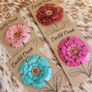 May include: Four leather flower pins in shades of pink, red, and turquoise, each with a copper center. The pins are attached to brown cards with the text "Cactus Creek Genuine Leather."