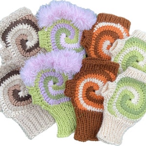 May include: A collection of colorful, handmade fingerless gloves. The gloves feature a spiral design in various colors, including brown, orange, green, and purple. Some gloves have a fluffy pink trim. The gloves are made of a knitted or crocheted material.