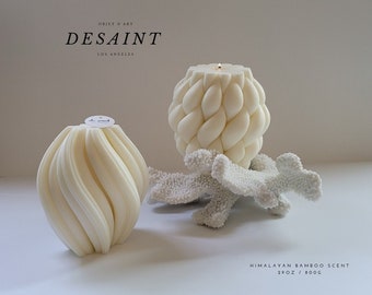 May include: Two ivory-colored candles with unique designs. One has a spiral pattern, the other a woven texture. A white coral-like object is between them. The text "OBJET D'ART DESAINT LOS ANGELES" is at the top. The text "HIMALAYAN BAMBOO SCENT 29OZ / 800G" is at the bottom.