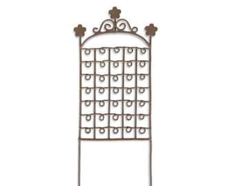 May include: A rustic metal garden trellis with a decorative top and a grid of circular openings. The trellis is designed to support climbing plants.