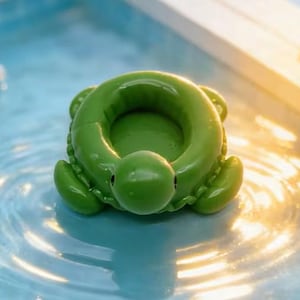 May include: A bright green turtle-shaped pool float. The float is in a pool of water, with the turtle's head and flippers visible. The float has a circular opening in the center.
