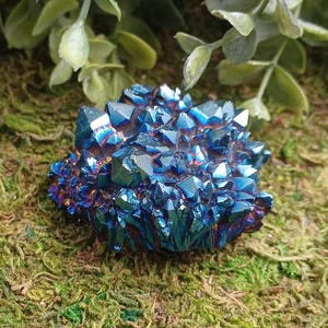 May include: A cluster of iridescent blue and purple titanium-coated quartz crystals. The mineral specimen features numerous sharp, pointed points with a metallic, reflective finish that shifts between deep cobalt, violet, and dark indigo hues.