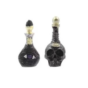 May include: Two black glass bottles with gold accents. One bottle is shaped like a skull and the other has an eye design. Both bottles have a dark liquid inside.