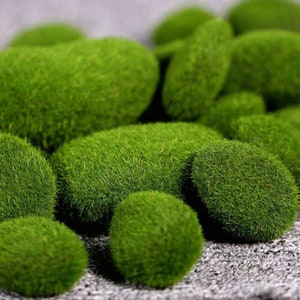 May include: A collection of green moss balls, resembling small, round rocks. The moss is a vibrant green and appears soft and fluffy.