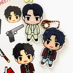 May include: Two acrylic character charms featuring chibi-style figures with dark hair. One figure wears a light yellow suit, and the other wears a maroon blazer with light blue pants. Both charms include a small metal ball chain for attachment.