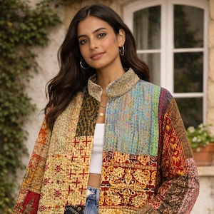 Op de afbeelding: Een patchworkjasje met een opstaande kraag. De jas heeft verschillende stoffen patches in rood, geel, blauw en bruin. De jas wordt gedragen met een witte top en een blauwe jeans.