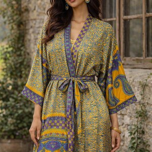 May include: A long, flowing kimono-style robe in shades of yellow, blue, and purple. The robe features a paisley and floral pattern, with a matching belt tied at the waist. The sleeves are wide and the robe has a V-neckline.