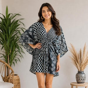 Op de afbeelding: Een korte kaftan-jurk met een V-hals en wijde kimono-mouwen. Het kledingstuk is versierd met een patchworkpatroon van zwart-witte geometrische vormen, waaronder stippen, concentrische cirkels en waaiervormige motieven.