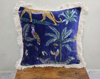 Op de afbeelding: Marineblau vierkant sierkussen met een jungle-thema, met een luipaard, toekans en een zebra. Het kussen heeft een crèmekleurige franjeborduur. Het ontwerp is gedrukt op een zachte, fluweelachtige stof.