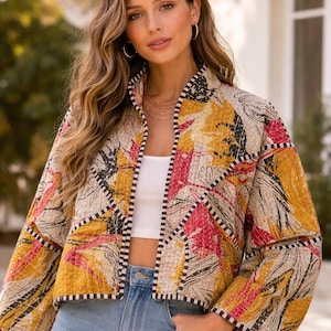May include: A quilted jacket with a vibrant floral pattern in yellow, pink, and black. The jacket has a stand-up collar and is trimmed with black and white striped fabric. The jacket is worn with a white top and blue jeans.