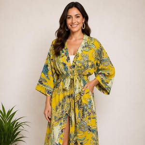 Könnte beinhalten: Ein gelber Kimono-Stil-Bademantel mit floralem Muster und Bindegürtel. Der Bademantel hat ein lebendiges Muster aus Blau, Grün und Weiß auf gelbem Hintergrund. Der Bademantel hat weite Ärmel und einen knielangen Saum, etwa 120 cm lang.