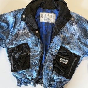 Peut inclure: Une veste matelassée réversible bleu et noire avec un motif tie-dye et le mot "CREAG" imprimé sur le devant. La veste a deux poches zippées sur le devant et une fermeture éclair.
