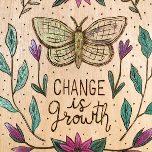 May include: A wooden plaque with a butterfly and floral design. The butterfly is in the center, with the words "CHANGE is GROWTH" below it. The design includes purple and green flowers and leaves.