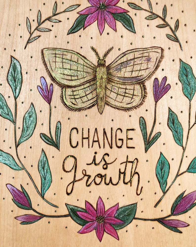 May include: A wooden plaque with a butterfly and floral design. The butterfly is in the center, with the words "CHANGE is GROWTH" below it. The design includes purple and green flowers and leaves.